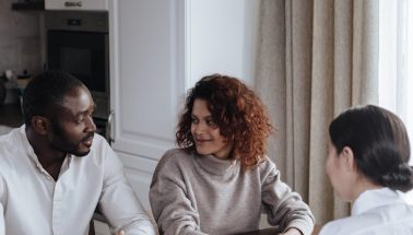 couple-looking-at-each-other-9870151 A diverse couple discusses with a consultant at home, capturing a casual business meeting.
